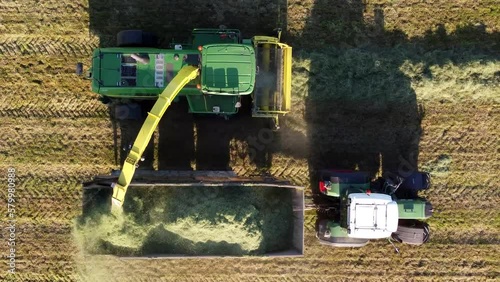 Aerial drone view of combine harvester picking up dried grass and unloading it into tractor chaser bin typical agriculture farming seen during beautiful summer evening 4k high resolution quality
