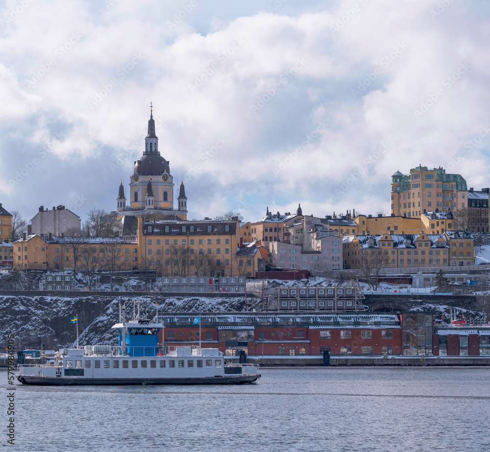 Harbor shuttle ferry passing the museum Fotografiska and the block at the church Katarina in the district Södermalm, a snowy day in Stockholm