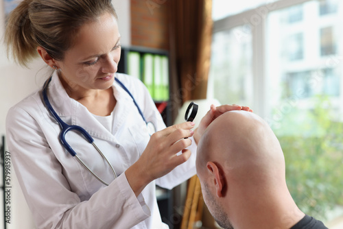 Behang Doctor checks scalp of bald male patient in medical clinic.
