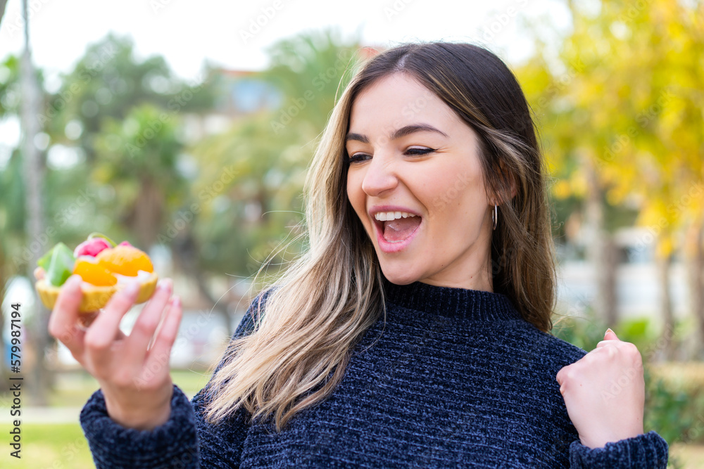 Young pretty Romanian woman holding a tartlet at outdoors celebrating a victory Young pretty Romanian woman holding a tartlet at outdoors celebrating a victory