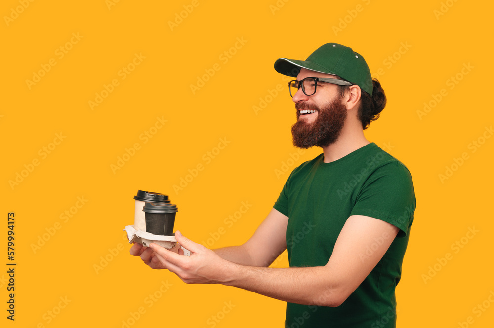 Friendly delivery bearded man in green uniform is handing two coffee cups. Friendly delivery bearded man in green uniform is handing two coffee cups.