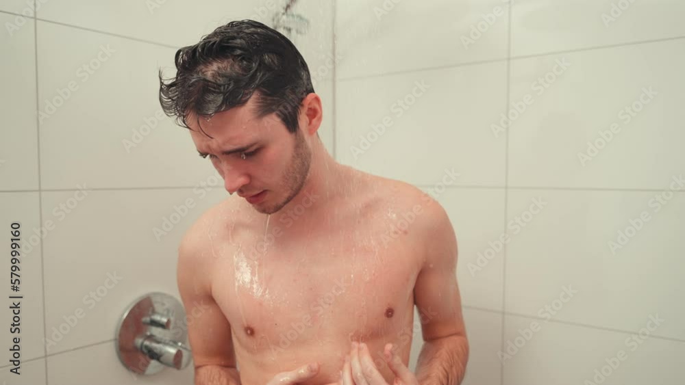 Young man taking a cold shower to stimulate circulation and promote health, feeling chilly but invigorated. Young man taking a cold shower to stimulate circulation and promote health, feeling chilly but invigorated.