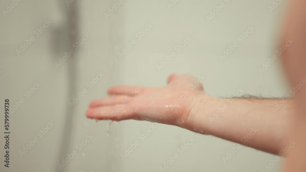 A man feeling the water temperature with his hand before taking a shower. A man feeling the water temperature with his hand before taking a shower.