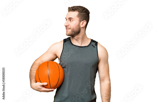 Handsome young man playing basketball over isolated chroma key background looking side