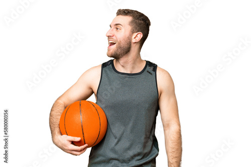 Handsome young man playing basketball over isolated chroma key background laughing in lateral position