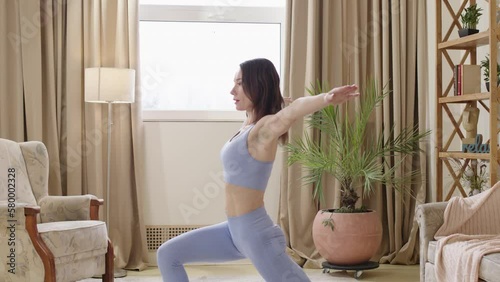 lady with toned body in sports clothes doing pilates in bright living room. sports woman doing yoga exercises stretching hands up and stretching legs. side view. Details of mushi and muscular body photo