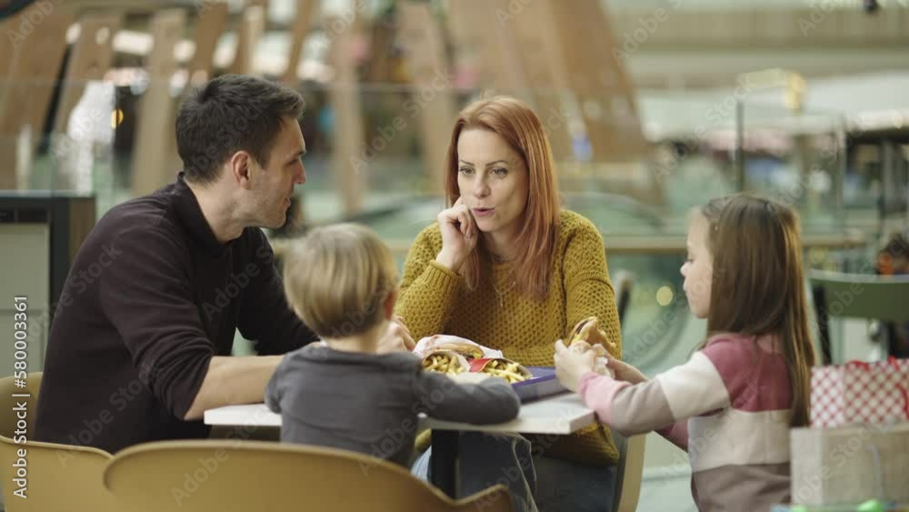 Cheerful parents and kids eating together and talking with each other at caf� in shopping mall. Shot in slow-motion Cheerful parents and kids eating together and talking with each other at caf� in shopping mall. Shot in slow-motion