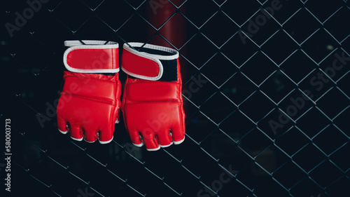 Red Gloves for MMA Boxers fighter hang on ring octagon black wall. Concept sport banner
