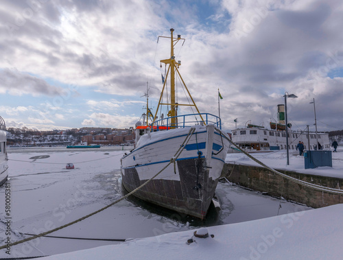 Old snowy fishing boat at the pier Norrmälarstrand on the island Kungsholmen and the bay Riddarfjärden with ice flows, a snowy day in Stockholm © Hans Baath