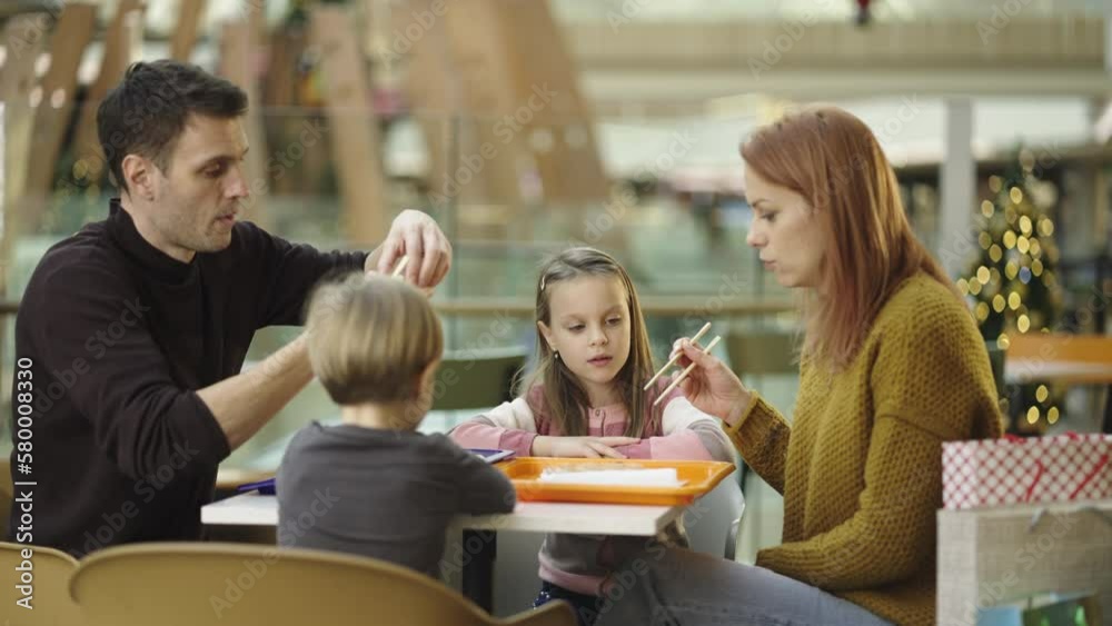 Family members in a restaurant, eating rolls with chopsticks in slow-motion. Kids learning how to eat with chopsticks Family members in a restaurant, eating rolls with chopsticks in slow-motion. Kids learning how to eat with chopsticks