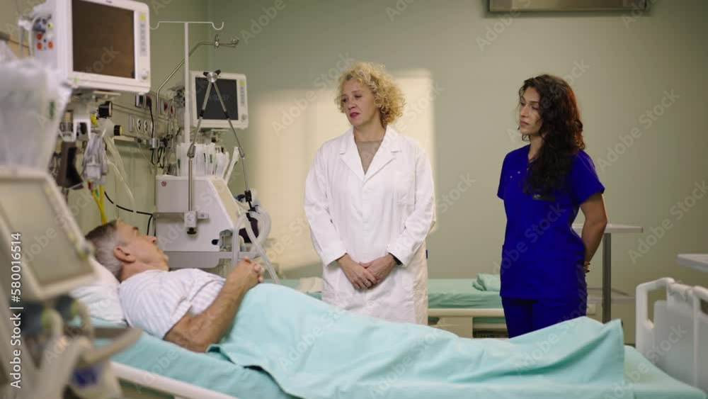 Slow-motion shot of a mature female doctor and her nurse talking to a mature male patient lying in a hospital bed Slow-motion shot of a mature female doctor and her nurse talking to a mature male patient lying in a hospital bed