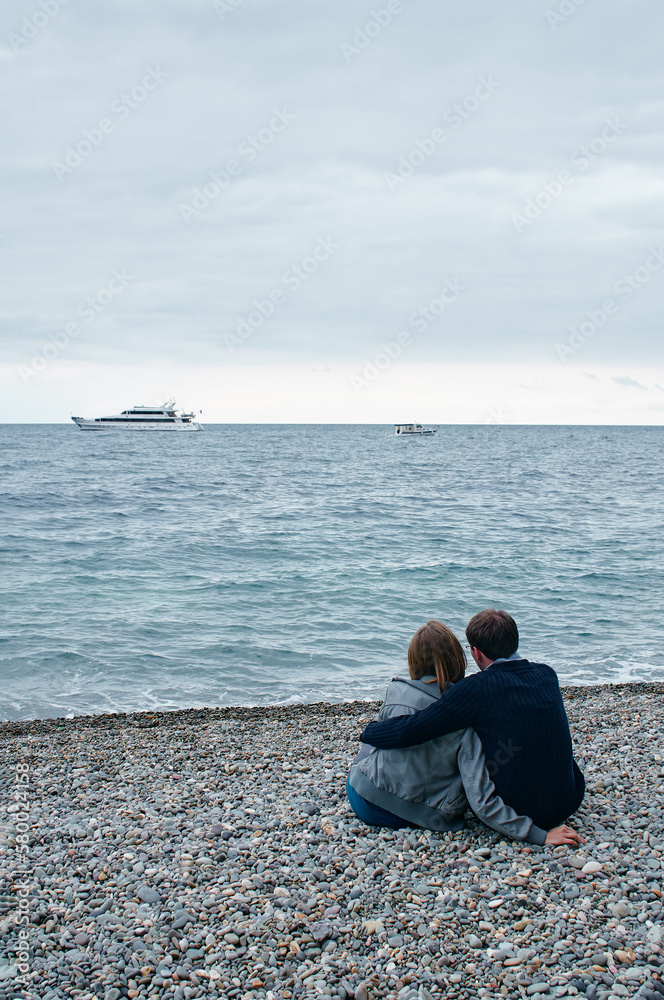Young loving couple sitting together on the beach enjoying the sea view.