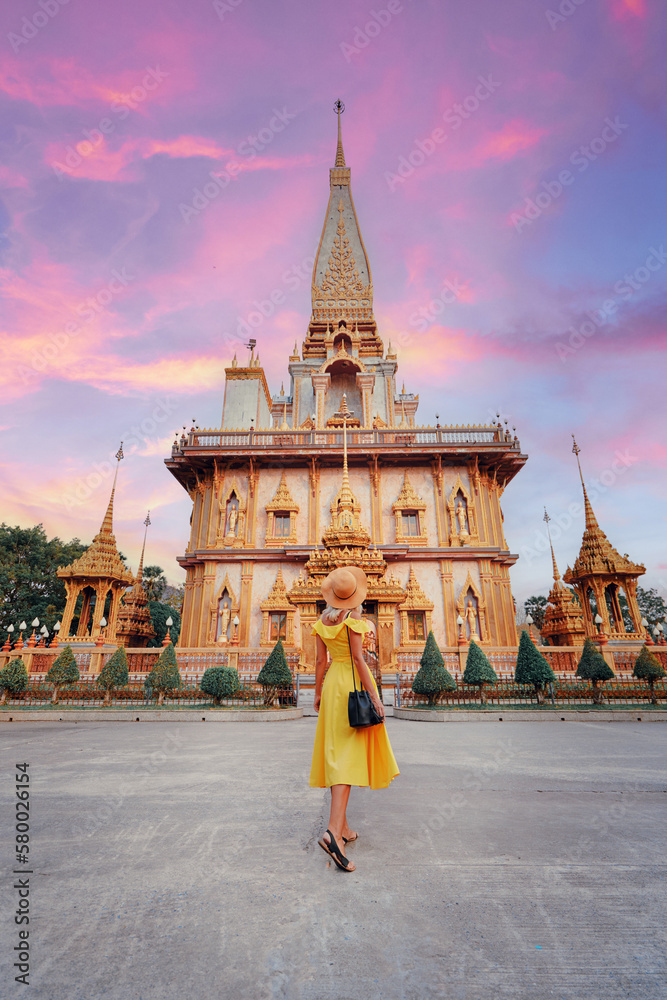 Travel by Asia. Young woman in hat and yellow dress walking near the Chalong buddhist temple on Phuket Island in Thailand. - obrazy, fototapety, plakaty 