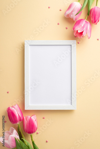 Mother's Day celebration concept. Top view vertical photo of empty photo frame bouquets of pink tulips and heart shaped sprinkles on isolated pastel beige background with copyspace