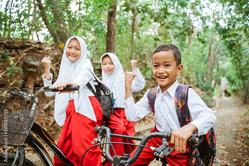 three elementary school students riding their bike through the country road and clenched their hand