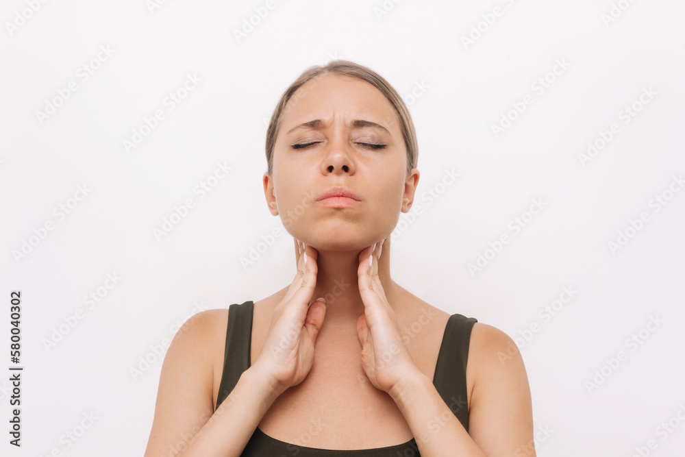 Young caucasian blonde woman with throat ache touches enlarged lymph nodes under jaw on her neck isolated on white background. Flu, cold, covid, tonsillitis, sars virus, inflamed tonsils. Sore throat Young caucasian blonde woman with throat ache touches enlarged lymph nodes under jaw on her neck isolated on white background. Flu, cold, covid, tonsillitis, sars virus, inflamed tonsils. Sore throat