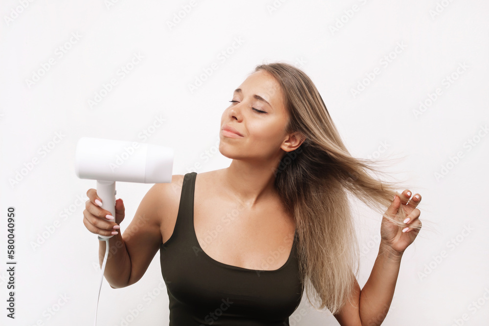 A young caucasian attractive blonde woman dries her hair isolated on a white background. Hair styling, damage A young caucasian attractive blonde woman dries her hair isolated on a white background. Hair styling, damage