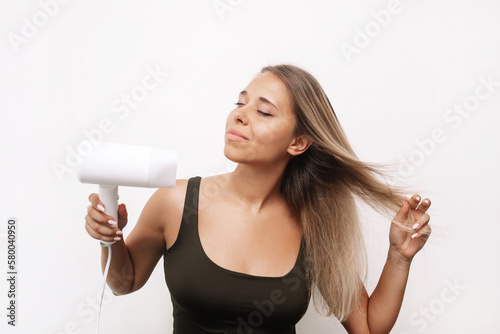 A young caucasian attractive blonde woman dries her hair isolated on a white background. Hair styling, damage