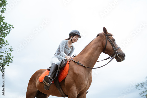 Female equestrian smiling while riding horse and holding reins in outdoor background © Odua Images