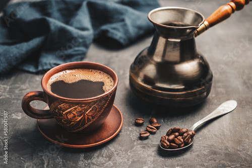 Black coffee drink in a clay cup, turkish jezve coffee pot and coffee beans in a spoon on dark background