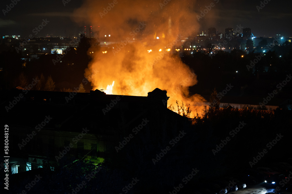 Building on fire at night in city. Orange flames and heavy smoke pouring out of burning damaged house during nighttime. Fire hazard in buildings concept
