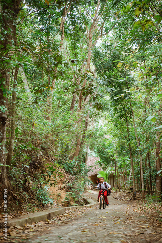 a male elementary student riding his bike through the country road alone with a lot of tree around him