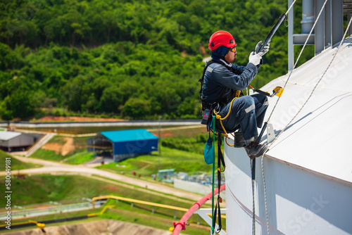 Focus male worker inspection wearing safety first harness rope safety line working at a high tank roof place on pipe