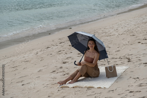 girl on the beach hiding from the sun under a large umbrella