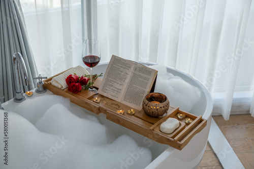 bamboo caddy on the bath tub with a glass of wine, a burning candle and a book