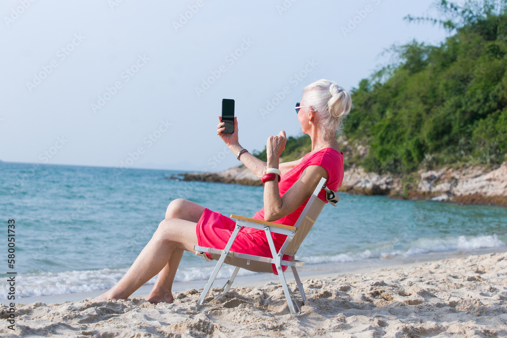 Happy Caucasian senior woman relaxing alone on beach chair on the beach over sunset. Retirement elderly female resting by the tropical sea relax and enjoy outdoor lifestyle activity in summer vacation Happy Caucasian senior woman relaxing alone on beach chair on the beach over sunset. Retirement elderly female resting by the tropical sea relax and enjoy outdoor lifestyle activity in summer vacation