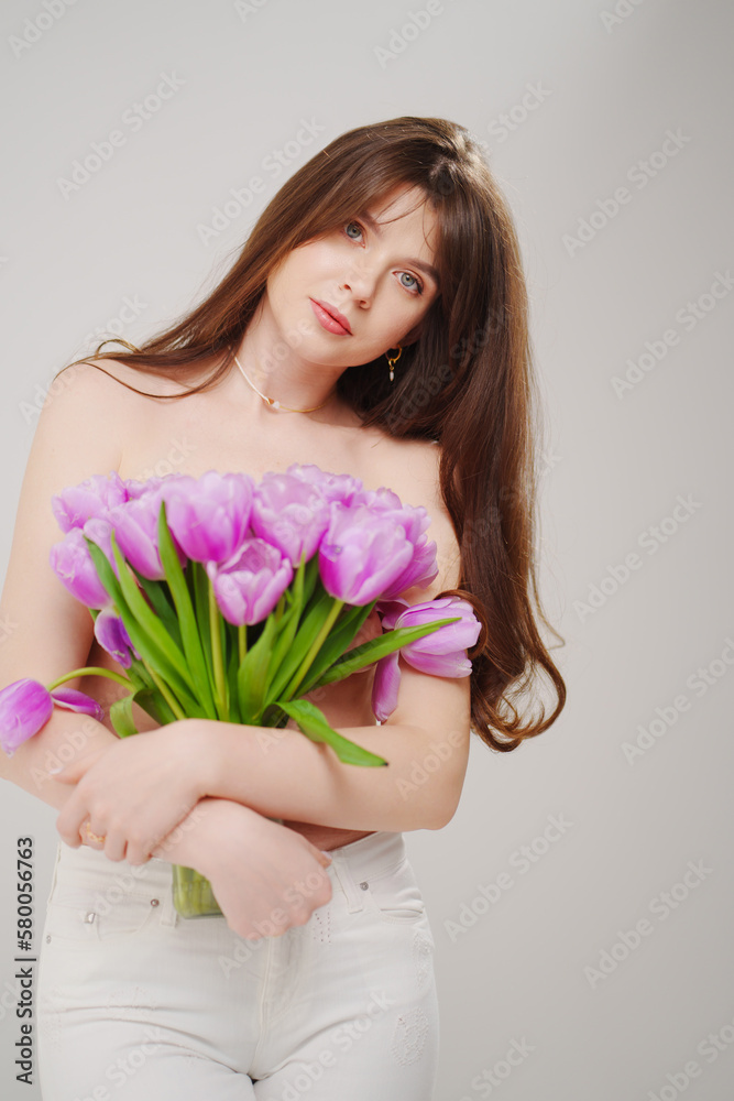 a gentle slim woman topless with tulips on a white background.