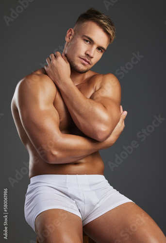 Thats one hunk of a man. Cropped portrait of a handsome and athletic young man posing shirtless in studio against a dark background. photo