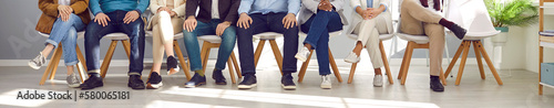 Cropped shot of group of job applicants sitting in row. Legs of diverse candidates, seekers sitting on chairs waiting for job interview in office. Human resources and employment