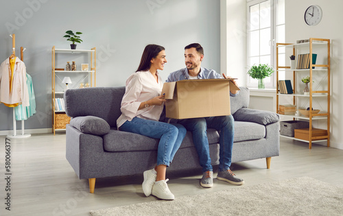 Excited young couple looking at each other while unpacking cardboard box at home. Man and woman customers unboxing parcel receiving online shop order or gift. Delivery and postal service concept © Studio Romantic