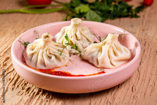 three khinkali with red sauce on a pink plate in a restaurant