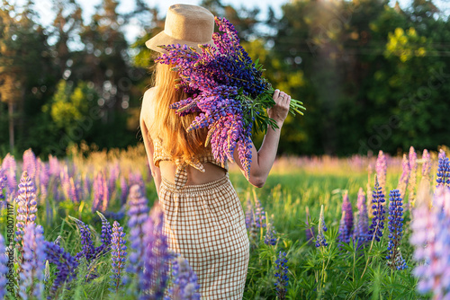 Beautiful Woman With Long Blond Hair in Straw Hat Walking in the Field With Lupins Flowers Summer Time
