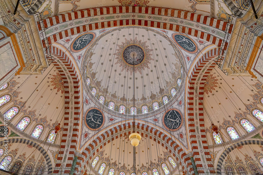 Interior of Fatih Mosque, a public Ottoman mosque in the Fatih district of Istanbul, with a huge decorated domes. Arabic text as decor (verses from Koran, muslim Holy book). Istanbul, Turkey