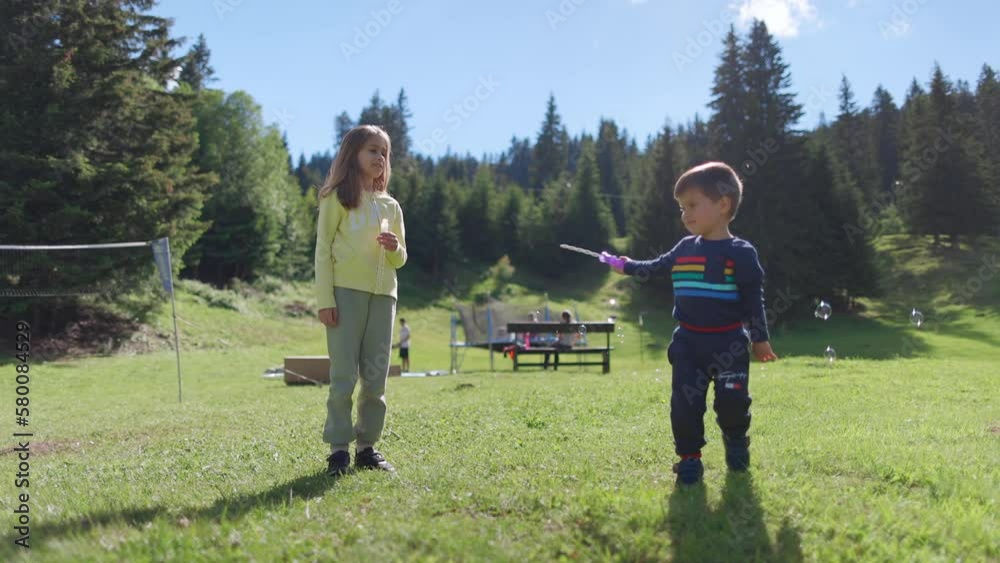 Older sister plays with younger brother and teaches him how to blow soap bubbles on the backyard in spring Older sister plays with younger brother and teaches him how to blow soap bubbles on the backyard in spring