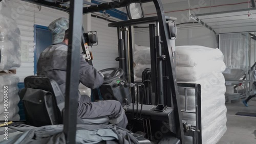 A man on an electric forklift stacks bags with pallets at a bakery. Adult Man works indoors on a forklift.