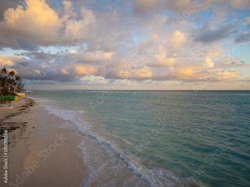 Beautiful seascape. There are gray storm clouds in the sky, a sandy beach, turquoise sea water with white foamy waves. Twilight. Nature, weather, recreation, tourism, ecology.