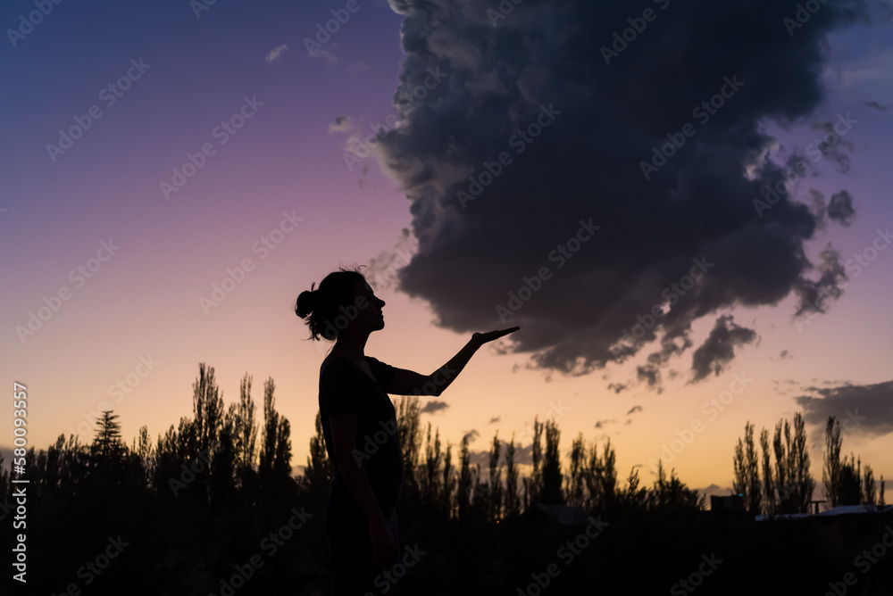 A woman is holding a cloud in front of a sunset.