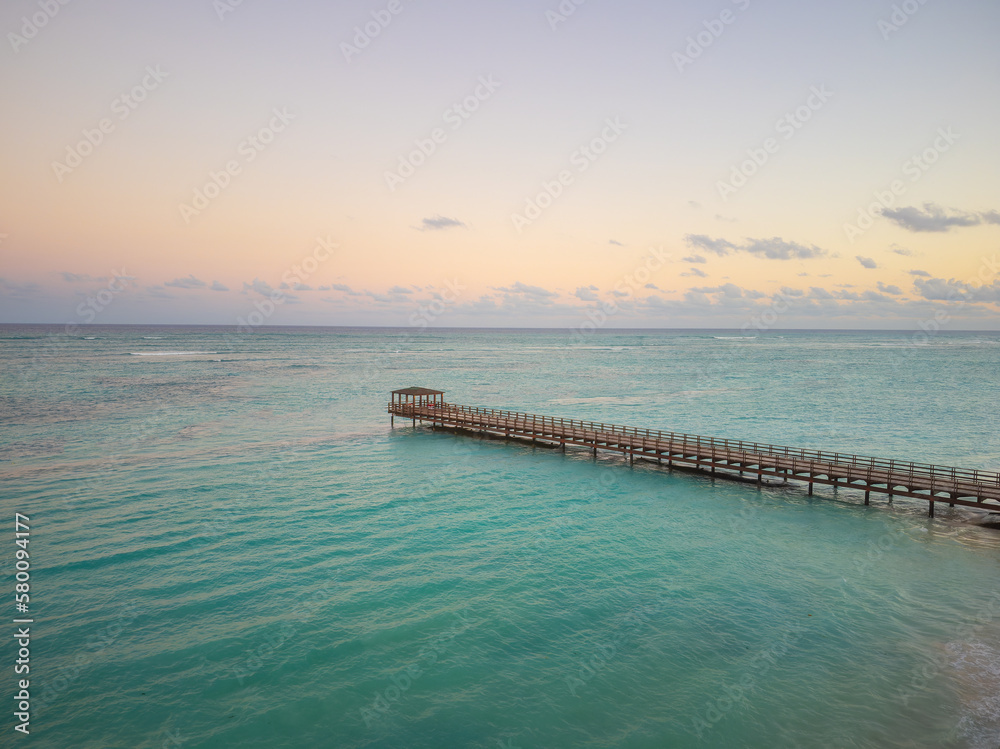 Wooden bridge in the sea. The sky with light clouds is colored with orange rays of the setting sun. Twilight. calm scenes. Vibrant seascape. There are no people in the photo.