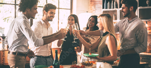 Group of happy young people cheering with champagne while having home party