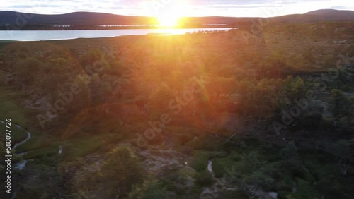 Sideways flight with a view of arctic wilderness and the midnight sun with fjells and a lake