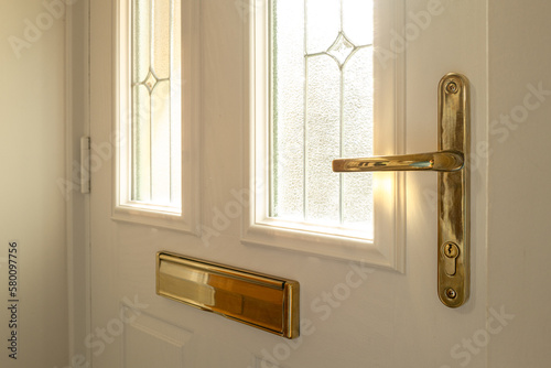 Shallow focus of a brass effect, new generation door lock and handle seen on a newly fitted, double glazed front door. Showing its double glazed, leaded windows.