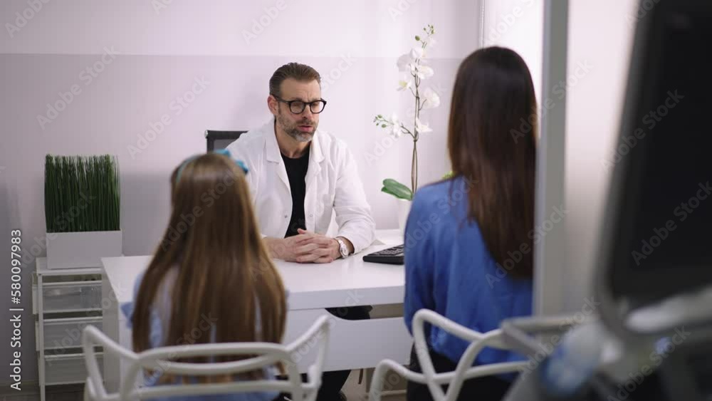 Friendly doctor sitting at the desk, talking to mother and child patient in his office Friendly doctor sitting at the desk, talking to mother and child patient in his office