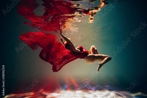 Art work. A slender, tanned girl with an athletic figure and blond hair, with red material and light underwear, in a ballet pose underwater in the pool. Aesthetic image for your design or decoration.
