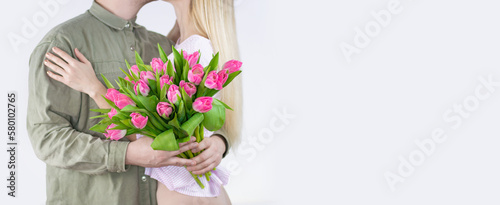 Young couple hugging with bouquet of tulips in hand isolated on white background. Space for text on the right