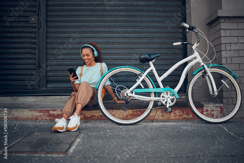 Fototapeta Naklejka Na Ścianę i Meble -  Bike, woman and headphone with phone in city relax, with bicycle and happy texting, social media apps and chat. Girl, lady and with eco friendly transportation, trendy or edgy look sit on sidewalk