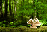 Old books lying on green moss in forest with trees in background. Open book with paper pages. Concept of knowledge, wisdom, fairy tales 